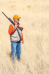 An adult male (upland game) hunter holding a shotgun standing in a field.