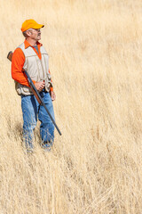 An adult male (upland game) hunter holding a shotgun standing in a field.