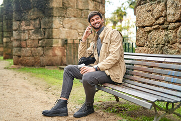 Smiling man sitting on bench and talking on smartphone
