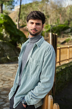Serious bearded male standing near wooden fence