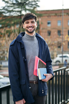 Smiling man with books standing in city park