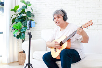 Asian elderly man Play music at home in the living room. Live Mobile broadcasting through applications on smartphones. The concept of playing music online. Modern communication. new lifestyle