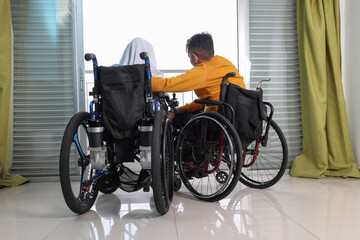 South east Asian malay man woman couple headscarf tudung middle aged disabled on wheelchair looking sitting in front of balcony window look outside