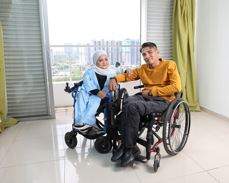 South east Asian malay man woman couple headscarf tudung middle aged disabled on wheelchair looking sitting in front of balcony window
