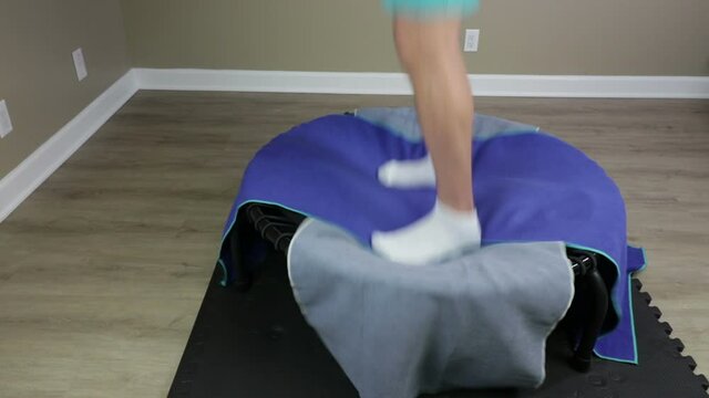 Mature caucasian man stepping onto a rebounder covered with two towels, exercising and then exiting. Adult white male exercising, bouncing and jogging on a rebounder or mini trampoline close-up.