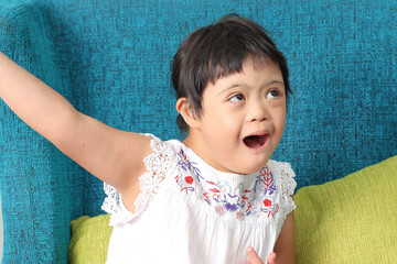 Southeast Asian child girl female special need medical down adhd autism syndrome look happy smile emotion expression open arms sing blue color sofa