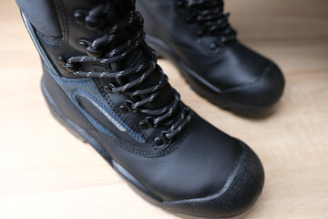 close-up of pair of new black work boots made of leather with reinforced cape, high top on wooden floor, concept of special protective professional shoes, professional work safety