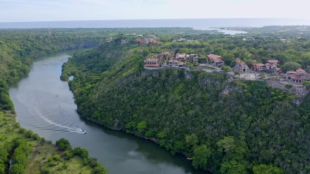 Aerial view of Altos de Chav&oacute;n Village with old ancient buildings and River Chavon with cruising boat on Dominican Republic