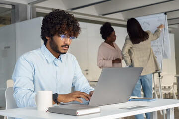 Serious indian man working on laptop at startup team open space office