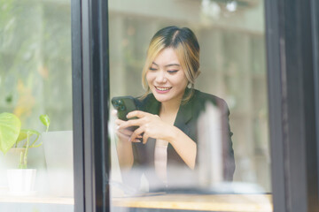 Smiling Asian woman sitting and using a smart phone in the cafe,Beautiful young girl working at a...