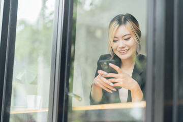 Smiling Asian woman sitting and using a smart phone in the cafe,Beautiful young girl working at a...