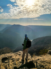 A hiker looks to the horizon with a beautiful landscape of mountains and dew