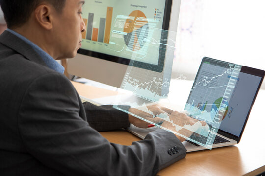 Asian businessman using laptop or computer notebook and desktop computer while analysing business performance and return on investment, ROI.