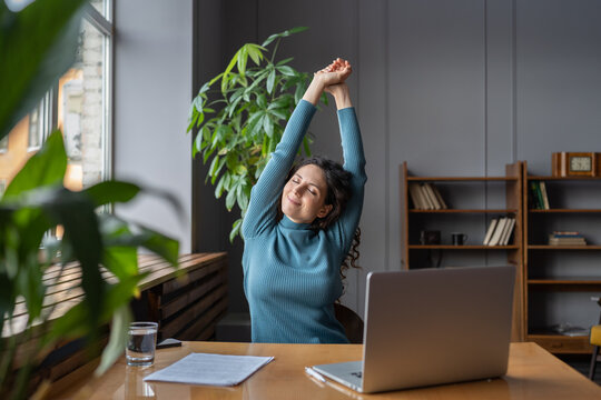 Happy businesswoman warming up body and muscles at workplace, feeling satisfied with work done, smiling female employee resting from computer screen. Well-being, productivity and happiness at work