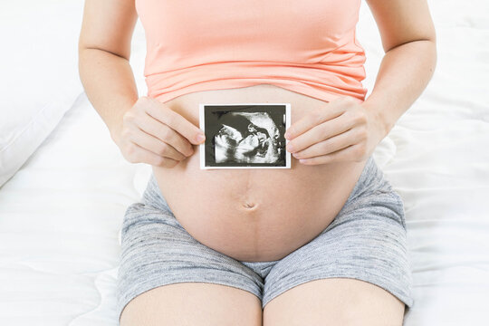 Soft focus and blurry of happy pregnant woman lying on bed at home holding and showing ultrasound scan photos. Pregnancy, Fetal examination, Antenatal Care, maternity, healthcare, parent and love.
