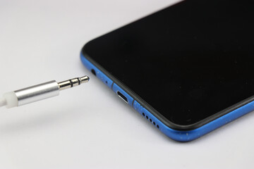 Connection of 3.5mm audio jack to a mobile phone on white background. Music concept