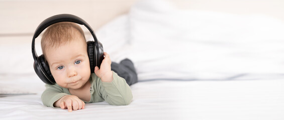 Pretty baby on a white background with headphones listening to music, baby 3 months old lying on bed with earphones, happy carefree childhood concept