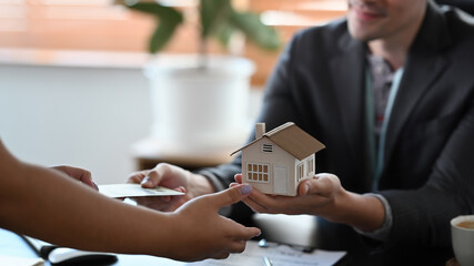 Cropped image of male estate agent holding house model and give proposal to customer.