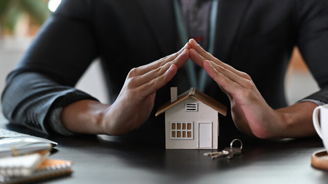 Estate agent hands over house model for protection and care. Property insurance concept.