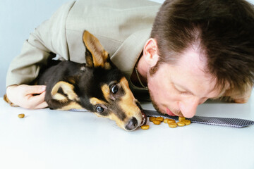 male volunteer playing with a dog from a kennel. they eat dog food together.