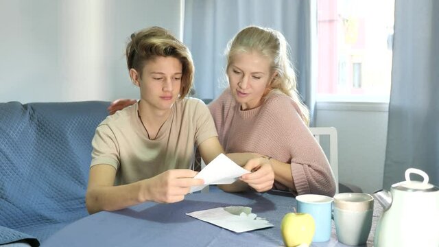 Upset mother and her teenager son read letter from school with test results, sitting indoor