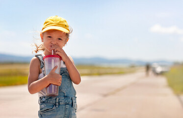 A little girl is drinking from a tube from a huge glass © Ольга Потылицына