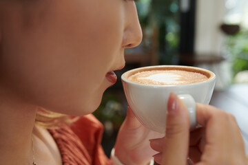 Closeup image of young woman drinking cup of delicious cappuccino