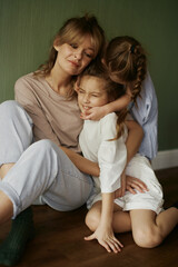 Mother and two funny daughters laughing and playing together. Sisters. Friendship. Family relationships. Green wall. Natural light. Love and happiness. Emotional and cute girls . Casual home clothes. 