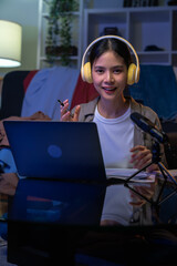 Cheerful beautiful Asian woman in a white t-shirt with wearing headphones and using laptop at video calling meeting and study online on the Internet.