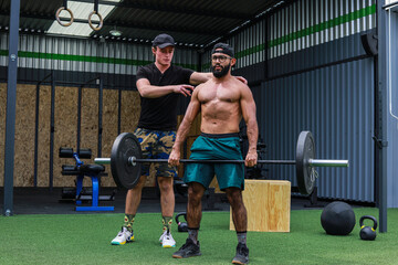 Fototapeta na wymiar Trainer teaching man to lift weights inside a crossfit GYM