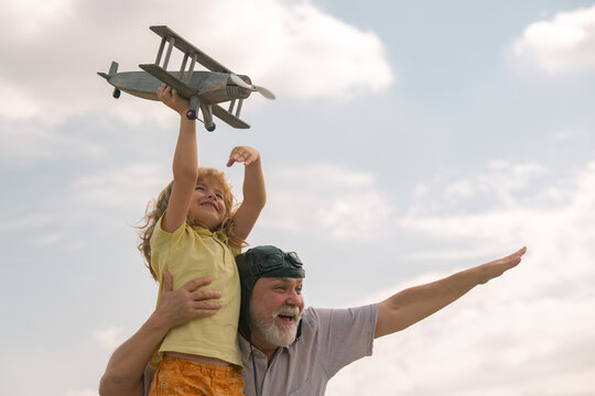 Excited child boy and grandfather having fun with plane outdoor on sky background with copy space. Child dreams of flying, happy childhood with grand dad.