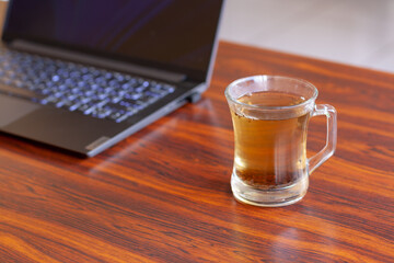 Tea mug with selective focus and laptop on blown table. Horizontal photo.