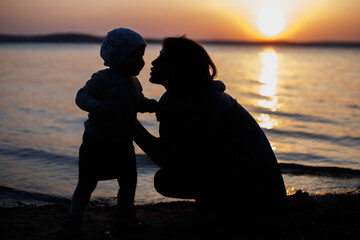 Fototapeta premium mom and daughter on the beach watching the sunset hugging and kissing