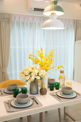 Stylish yellow setting on dining table with yellow flower vase in trendy interior.