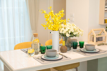 Stylish yellow setting on dining table with yellow flower vase in trendy interior.