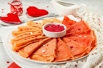 Thin red crepes or pancakes with raspberry sugar and sweet hearts pastry topping