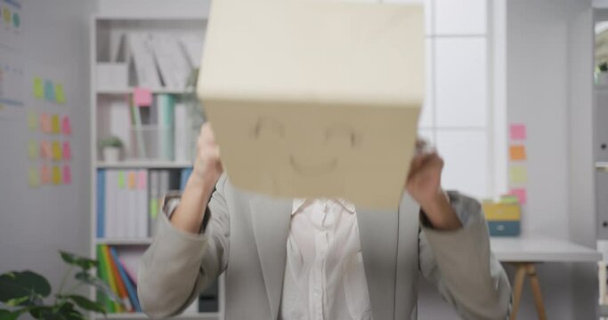 Young Asian businesswoman sit on desk wear draw smile mask paper bag hide feel bad mood with fail work at office. Anonymous young lady mad annoying and blame with overwork, Work mental health.