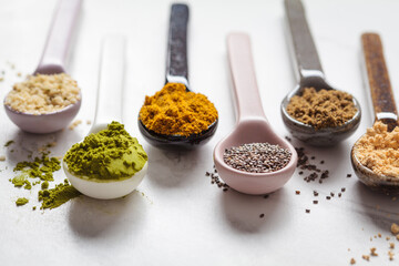 Super food powders in spoons, white marble background.