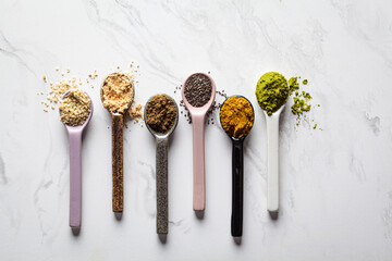 Super food powders in spoons, white marble background.