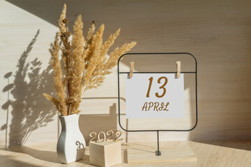 April 13. 13th day of month, calendar date. White vase with dead wood next to the numbers 2022 and stand with an empty sheet of paper on table. Concept of day of year, time planner, spring month