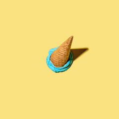 Dropped upside down ice cream cone with melting scoop on yellow background.