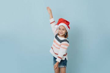 Obraz premium Happy little girl in christmas hat making dancing moves over blue