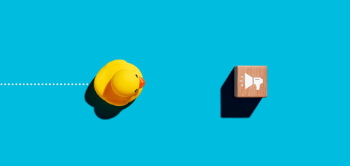 Toy robber duck moves towards a wooden cube with a megaphone icon. Help and support assistance service