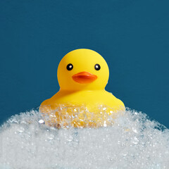 Yellow rubber duck toy floating on soap or shampoo bubble foam in the bath. Duckling in bubble bathtub with soapy foam.