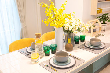 Stylish yellow setting on dining table with yellow flower vase in trendy interior.