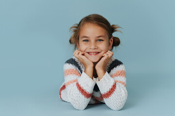 Portrait of a smiling little girl in striped sweater lying on floor over blue