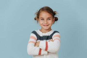 Confident smiling little girl in sweater standing with hands crossed