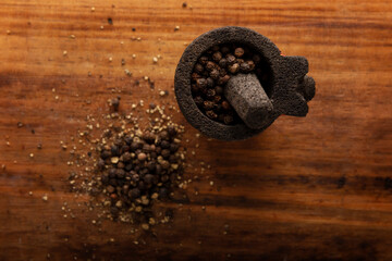 Black pepper grains in a small Molcajete (traditional Mexican version of the mortar and pestle) on rustic wooden background..Flat lay image. Close up