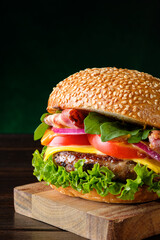 Fresh delicious burger close-up on dark green background with copy space, vertical composition. Fast food concept.