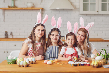 Happy easter. Mother and daughters with rabbit ears decorate Easter eggs sitting at a table in kitchen.